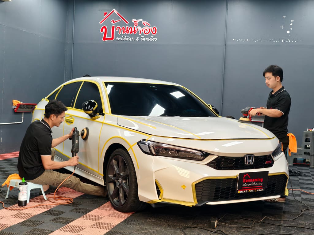 ช่างสองคนกำลังขัดสี Honda Civic สีขาวที่ปิดเทปกันขัดไว้ ในห้องทำงานของร้าน