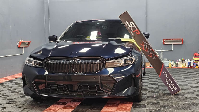 BMW 330Li สีเข้มหลังติดฟิล์มใสกันรอย พร้อมกล่องฟิล์ม SCP วางข้างรถ